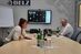 Stuckateurmeister Michael Christmann (r.) und seine Auszubildende Veronika Sadowski (l.) sitzen an einem Konferenztisch im Büro von Stuck Belz in Bonn. Vor ihnen stehen ein Laptop und ein Tablet. An der Wand hängt ein Bildschirm.  Darauf sind die 21 Teilnehmerinnen zu sehen, die am Girls'Day ein virtuelles Praktikum bei Stuck Belz gemacht haben.