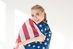 Eine junge Frau blickt mit leicht schräg gehaltenem Kopf in die Kamera. Sie lacht und hat sich eine amerikanische Flagge um ihre Schulter gewickelt.